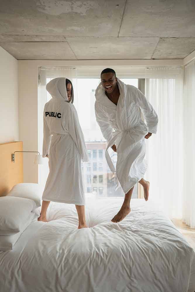 Couple jumping on bed in Public hotel robes