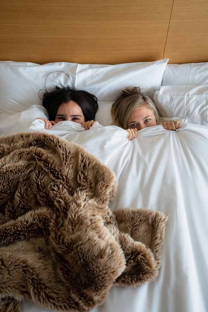 couple in bed with sheets pulled up covering half their face
